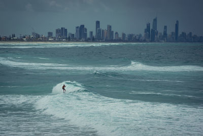 Eine person mitten in den wellen mit  surfen und im hintergrund surfers paradise. 