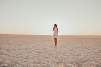 Rear view of woman standing at beach against clear sky