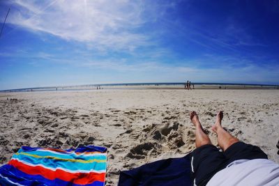 Low section of man on beach against blue sky