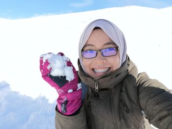 Portrait of cheerful woman holding snowball on mountain