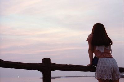 Rear view of woman standing on railing against sky