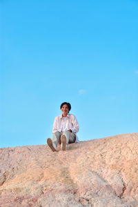 Low angle view of woman sitting on mountain against clear blue sky