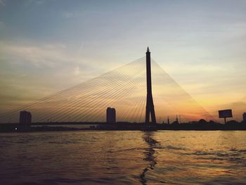 Suspension bridge over sea against sky during sunset