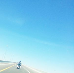 Man riding bicycle on road against clear blue sky
