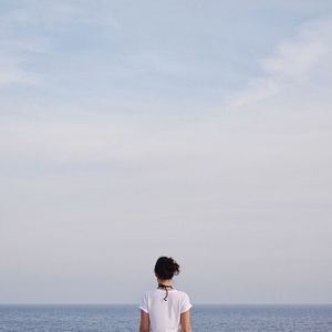 Rear view of woman standing in sea against sky