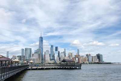 View of buildings in city by sea against cloudy sky