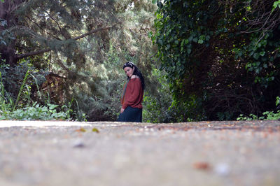 Portrait of young woman standing on footpath against trees in forest