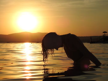 Woman in sea against sky during sunset