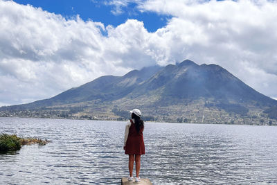 Rear view of woman standing by lake against sky