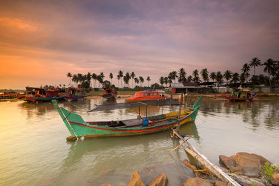 Boats moored in sea against sky during sunset