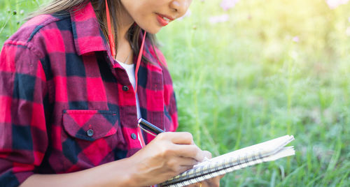 Midsection of woman writing in book while sitting on grass