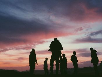 Silhouette people standing on mountain against cloudy sky during sunset