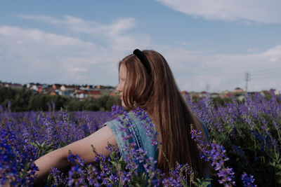 Woman standing by purple flowers on field against sky