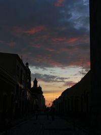 Silhouette buildings by street against sky during sunset