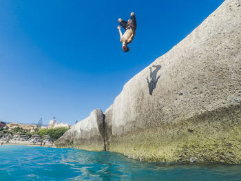 Boy jumping in sea against blue sky