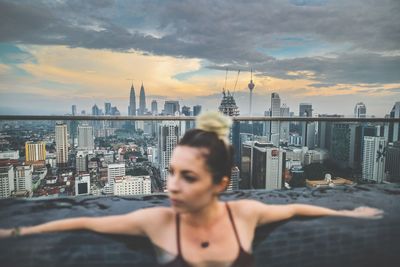 Young woman relaxing in infinity pool against cityscape