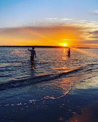 Silhouette people on beach against sky during sunset