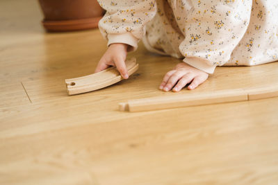 Toddler girl in white dress plays with wooden train at home in the living room