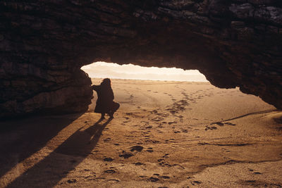 Silhouette young woman standing by rock formation at beach during sunset