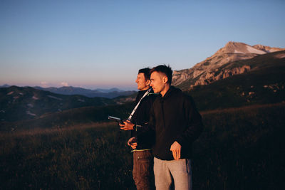 Man holding remote control of drone by friend against sky