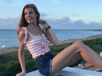 Portrait of smiling young woman sitting against sea