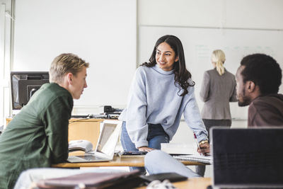 Smiling young woman talking with male student in classroom