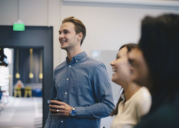 Happy businessman holding coffee cup while standing with colleagues in office