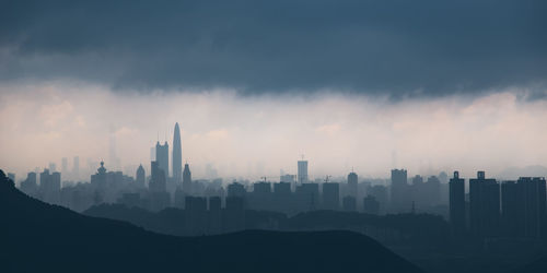 Silhouette skyscrapers in city against sky during foggy weather