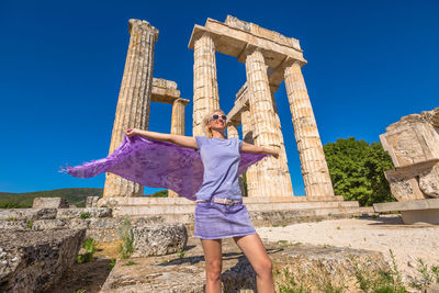 Woman with arms outstretched standing against old built structure