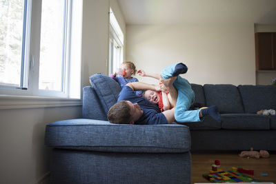 Happy father playing with son while daughter drinking water on sofa at home