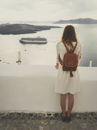 Rear view of woman standing on sea shore against sky with cruise ship