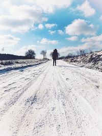 Rear view of person walking on snow covered road against sky