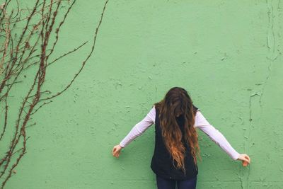 Young woman standing against green wall