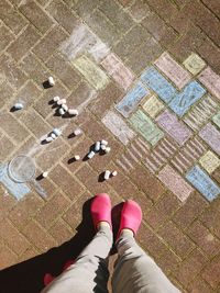 Low section of person standing on tiled floor by chalks and drawing on footpath