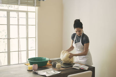 Woman kneading dough while reading recipe in book at table