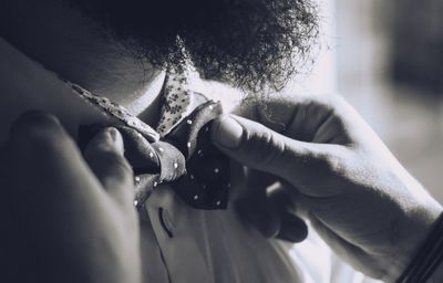Cropped image of person adjusting bowtie of man