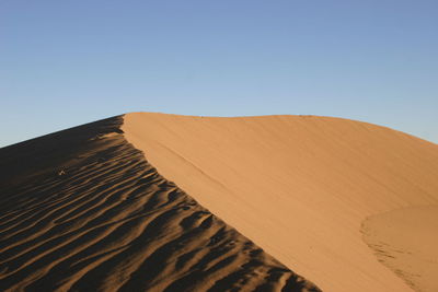 Sunlight falling on sand dune at desert against clear sky