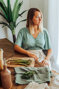 Young caucasian woman in apron sitting at kitchen table resting