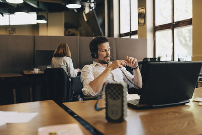Creative businessman wearing headphones while video conferencing on laptop in office