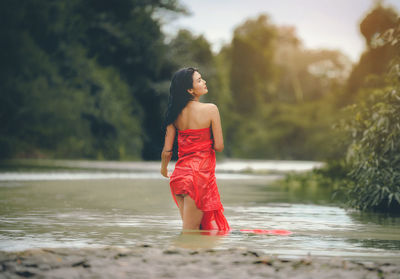 Young woman looking away while standing by trees