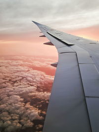 Airplane wing flying over sunset pink cloudy sky