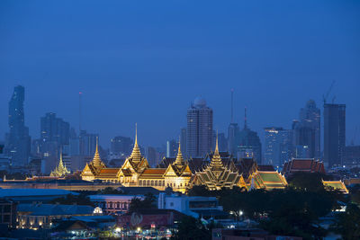 Illuminated cityscape against clear blue sky at night