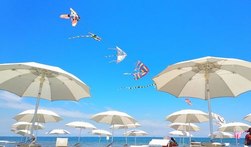 Low angle view of umbrellas hanging on beach against clear blue sky