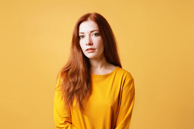 Portrait of young woman standing against yellow background