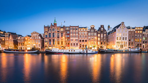 Buildings by river against clear blue sky