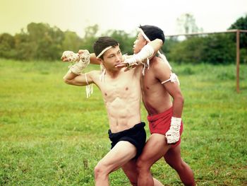 Shirtless male fighters practicing on grass against sky
