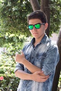 Young man wearing sunglasses standing against tree