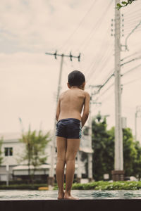 Rear view of boy jumping in swimming pool against building in city