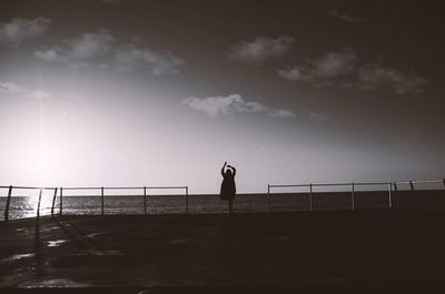 Silhouette woman standing on promenade by sea against sky