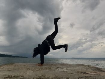 Woman doing handstand on pier over sea against sky